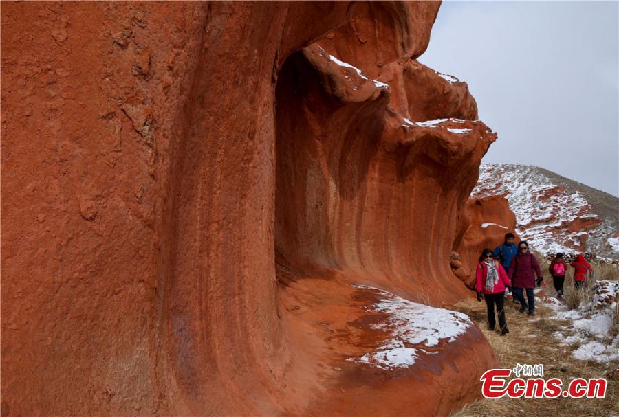 Tourists visit the snow-covered Danxia landform in Sunan Yugur Autonomous County, Northwest China\'s Gansu Province during the Spring Festival holiday. The Danxia landform is a unique type of geomorphology formed from red-colored sandstone and characterized by steep cliffs. (Photo: China News Service/Wang Jiang)